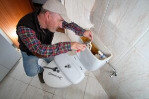Man repairing a toilet tank with tools on the closed toilet seat.