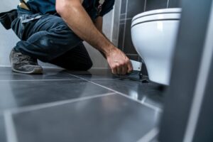 Person installing or adjusting a toilet on a tiled bathroom floor.