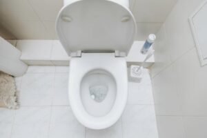 White toilet bowl with open lid and a toilet brush holder on a tiled bathroom floor.