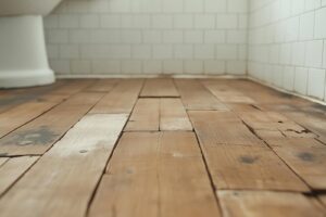 Worn wooden floorboards with visible cracks and discoloration in a bathroom.