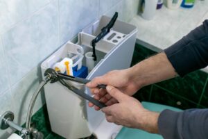 Hands using pliers to repair the inside of a toilet tank.