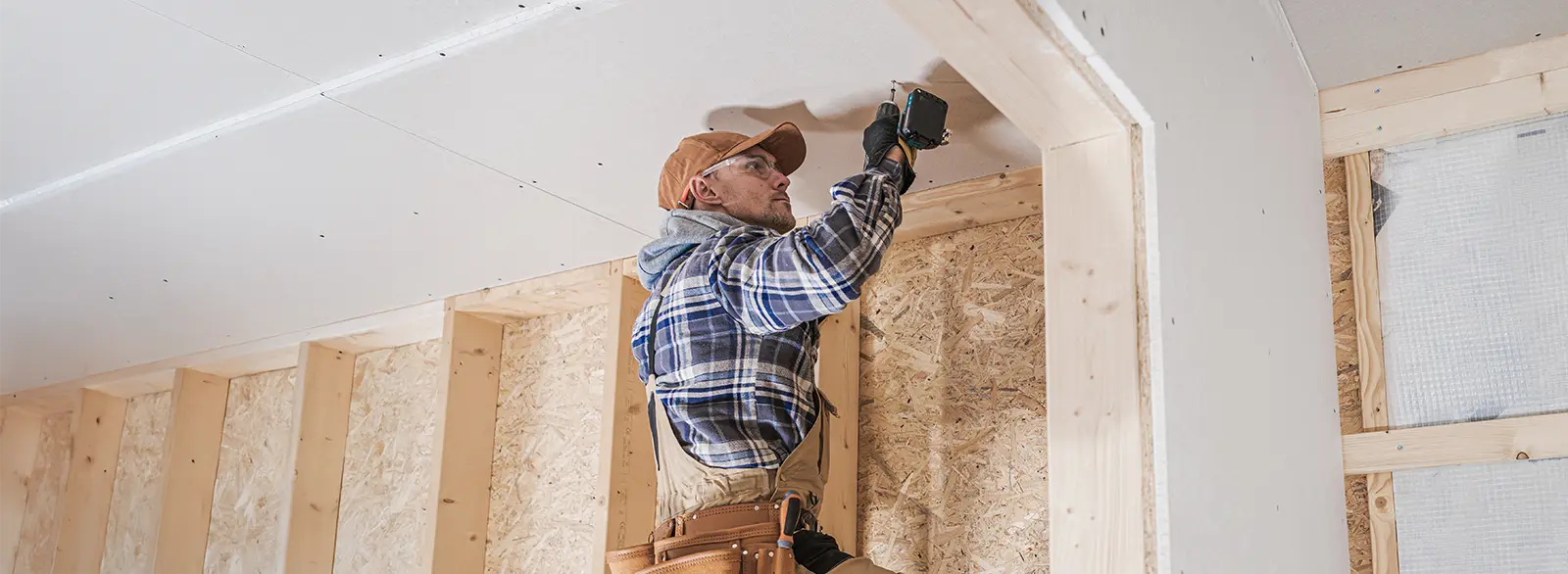 Drywall panel being fastened to framing overhead during a water damage repair