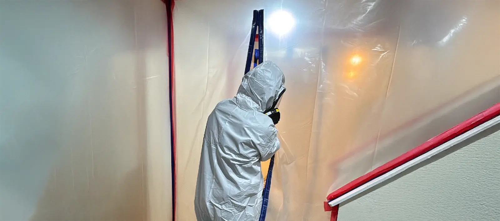 Prime Restore Solutions technician in a protective suit and respirator inside a plastic containment area during mold remediation
